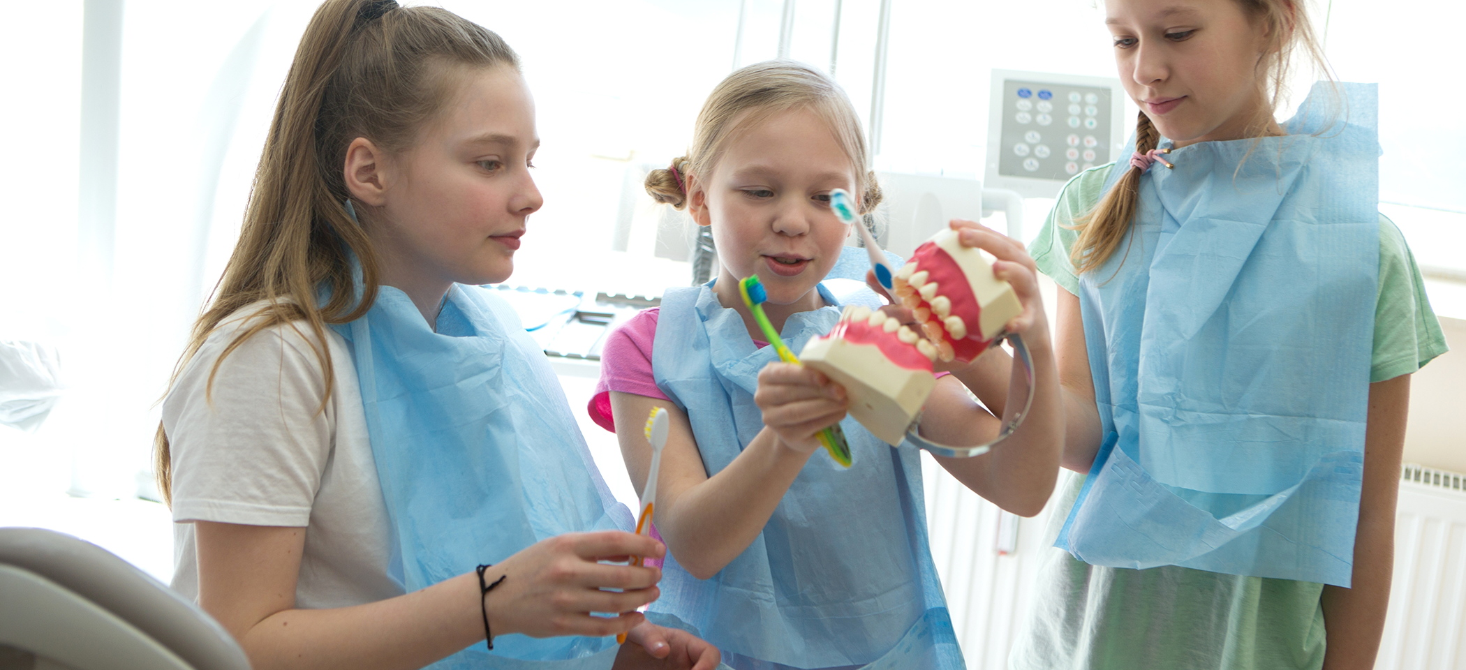 Three young girls looking at a model of the teeth in a dental office