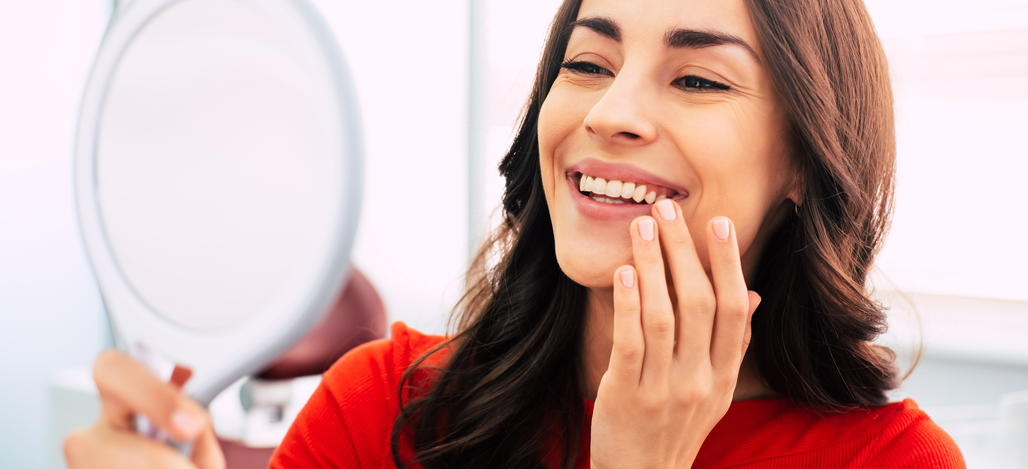 Woman looking at her smile in a mirror after cosmetic dentistry in Cleburne