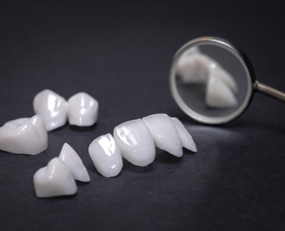 Several white dental crowns and veneers next to a dental mirror