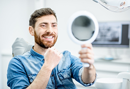 Man in dental chair admiring his smile in a mirror