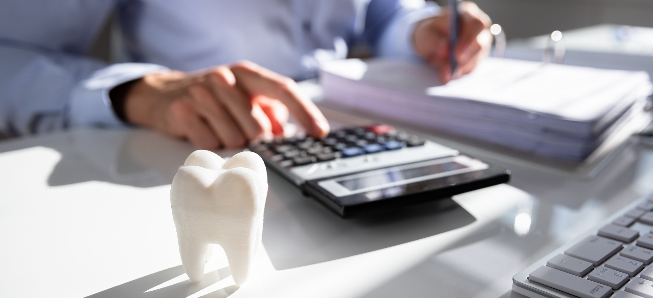 Person typing on a calculator while filling out dental insurance paperwork