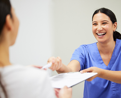 Smiling dental team member handing a clipboard to a patient