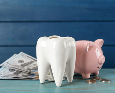 Pink piggy bank with money next to a model of a tooth