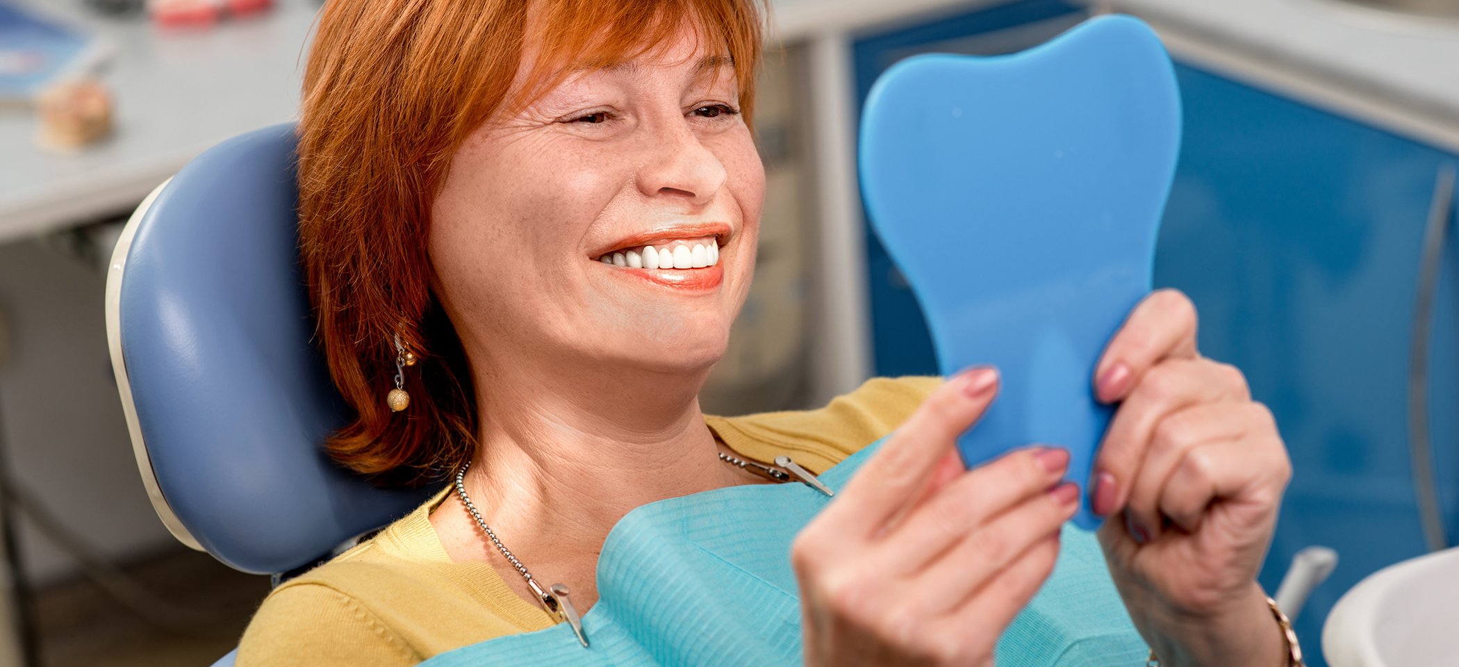 Woman looking at her smile in a mirror after restorative dentistry in Cleburne